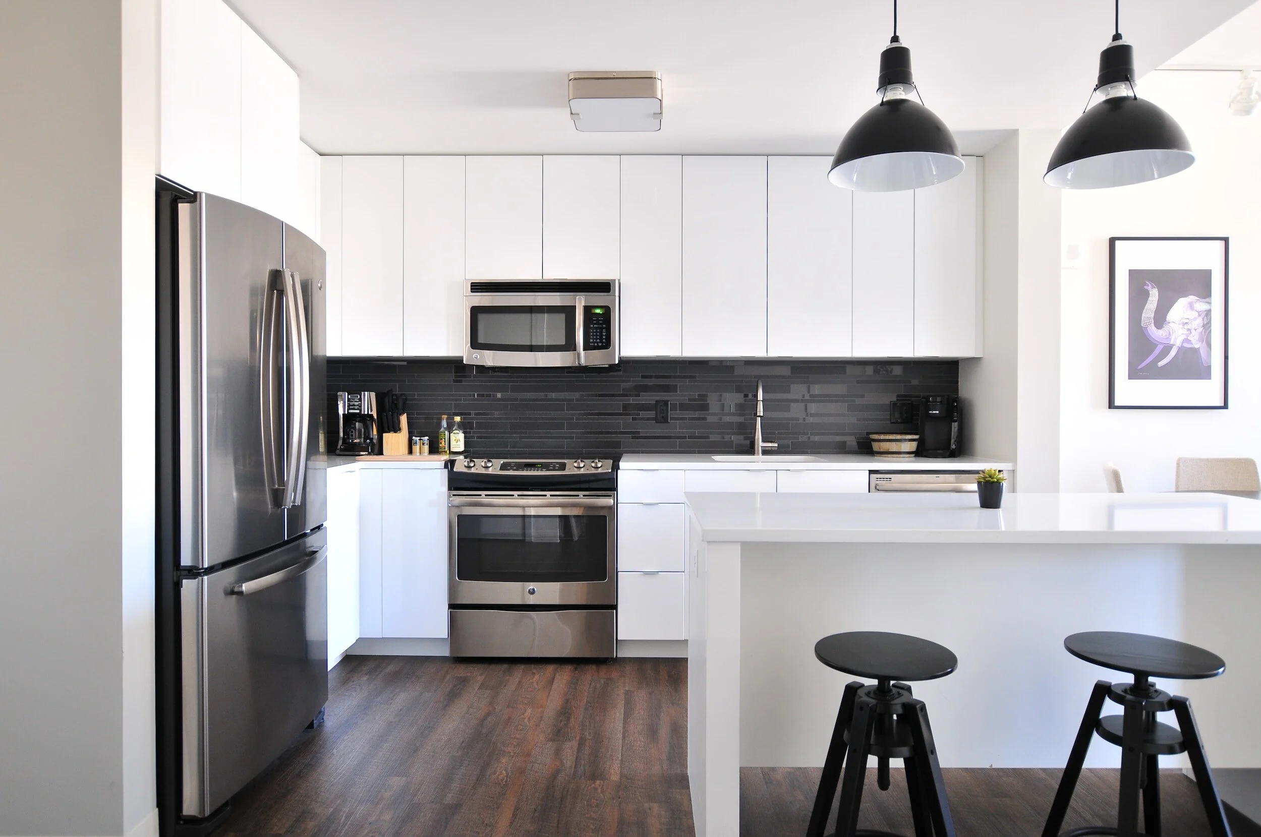 Bright, modern kitchen with white cabinetry, dark pendant lighting, and wood flooring